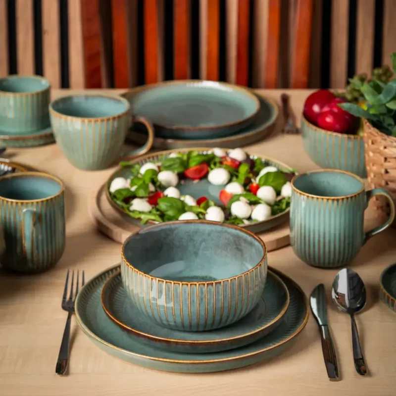 Talerze i filiżanki z porcelany w turkusowym odcieniu z złotymi detalami na drewnianym stole, idealne do domowego użytku i aranżacji wnętrz w stylu rustykalnym, dodające ciepła i elegancji.