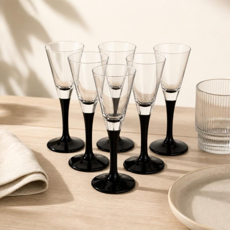 Przezroczyste kieliszki do szampana z czarną podstawą, eleganckie szkło na uroczystości, na stole z białą tkaniną i ceramicznymi naczyniami, nowoczesny design.