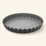 Czarna forma do tarty z falistymi krawędziami, idealna do pieczenia i serwowania wypieków, wykonana z wysokiej jakości materiałów ceramicznych i metalowych.