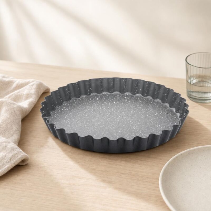 Czarna taca ceramiczna z falistymi krawędziami na drewnianym stole, obok szklanka wody i biały talerz, minimalistyczny wystrój kuchni, domowe akcesoria kuchenne, nowoczesny design.