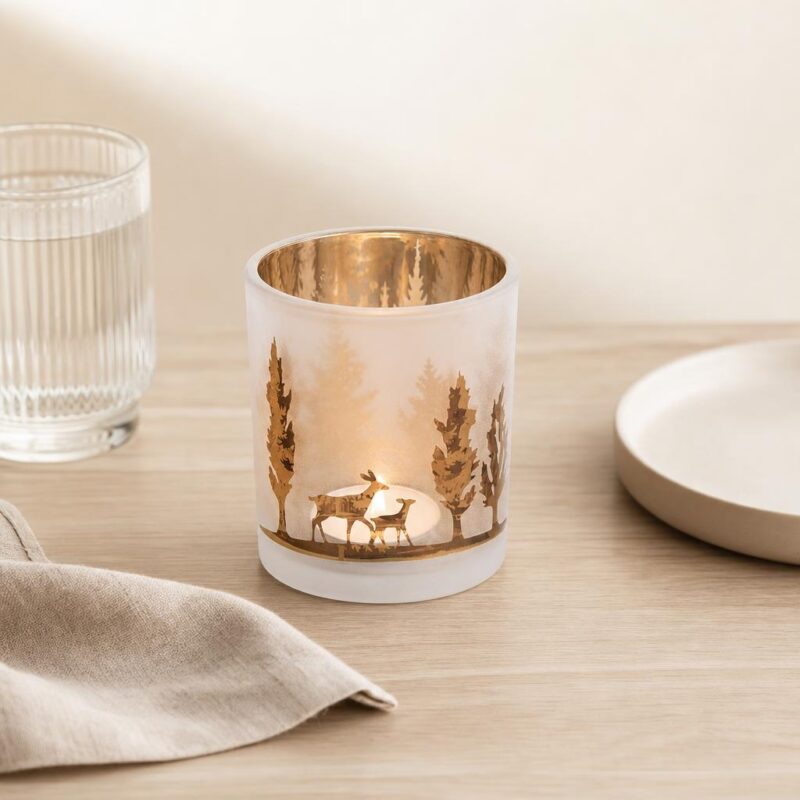 Przedmiotowa świeca w szklanym lampionie z złotym wnętrzem, dekoracja na stół, otoczona talerzami i szklankami, idealna do kuchni i jadalni, element wystroju wnętrz, elegancka i stylowa.